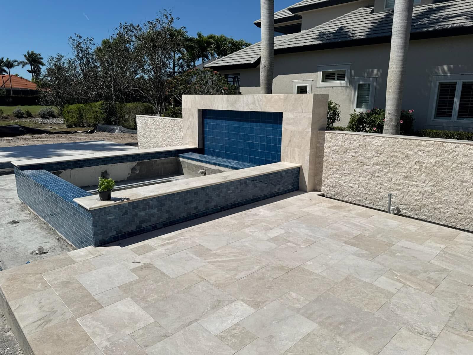Modern patio with stone pavers, raised planter, and a blue water feature beside a house