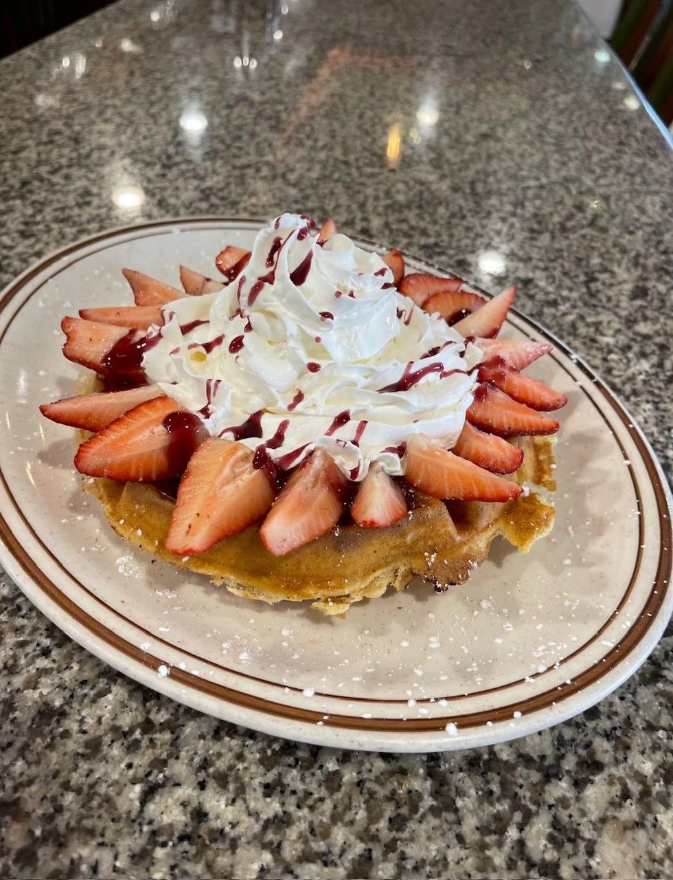 A waffle with strawberries and whipped cream on a plate on a table.
