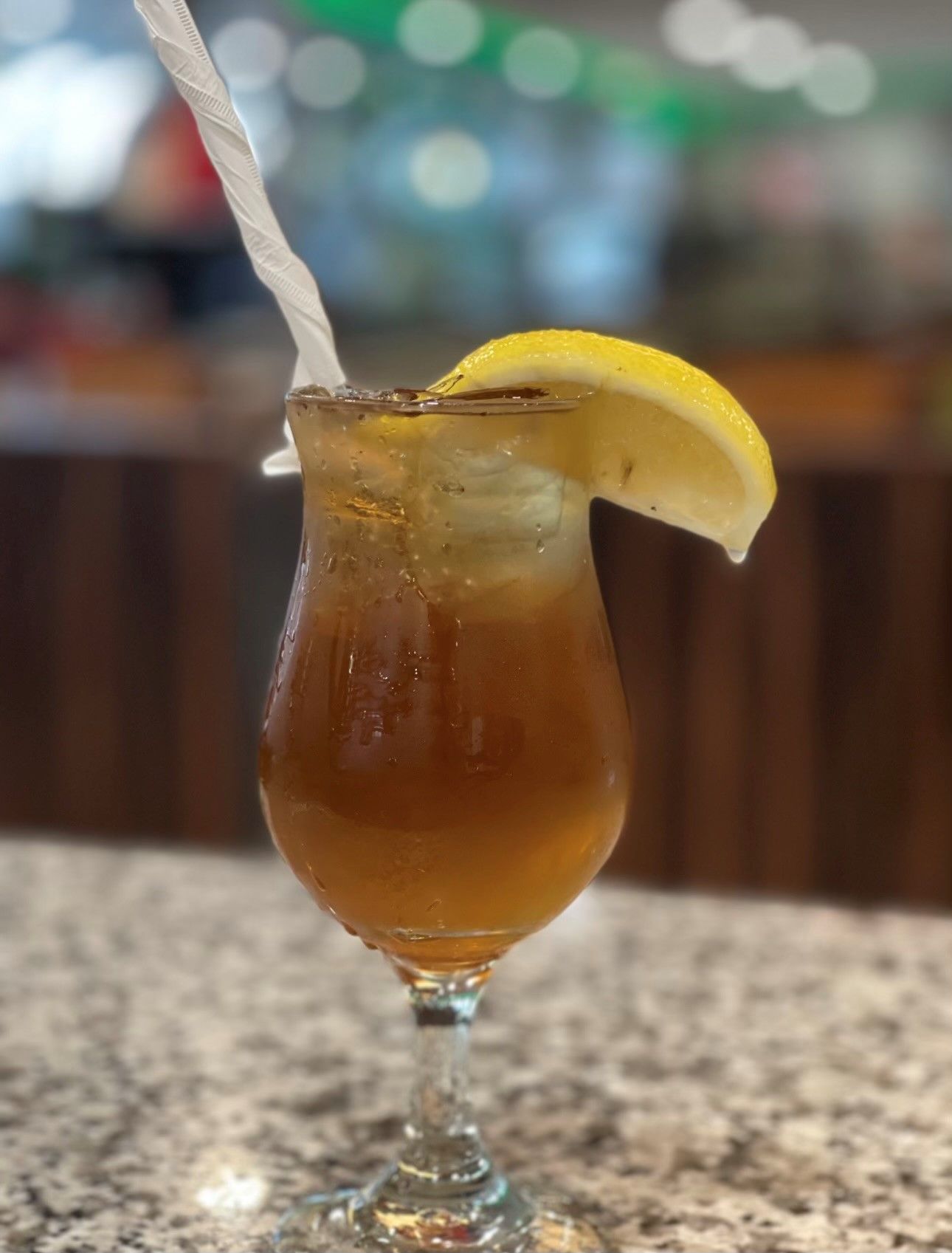 A glass of iced tea with a lemon slice and a straw on a table.