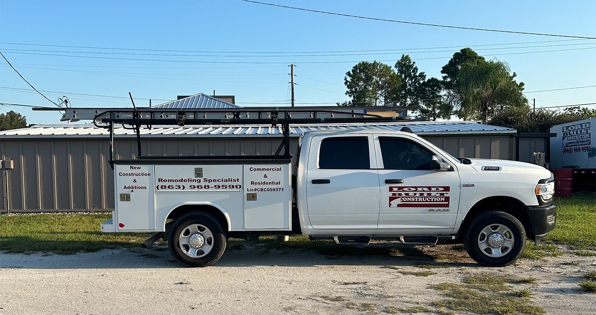 A white truck with a ladder rack on the back is parked in a parking lot.
