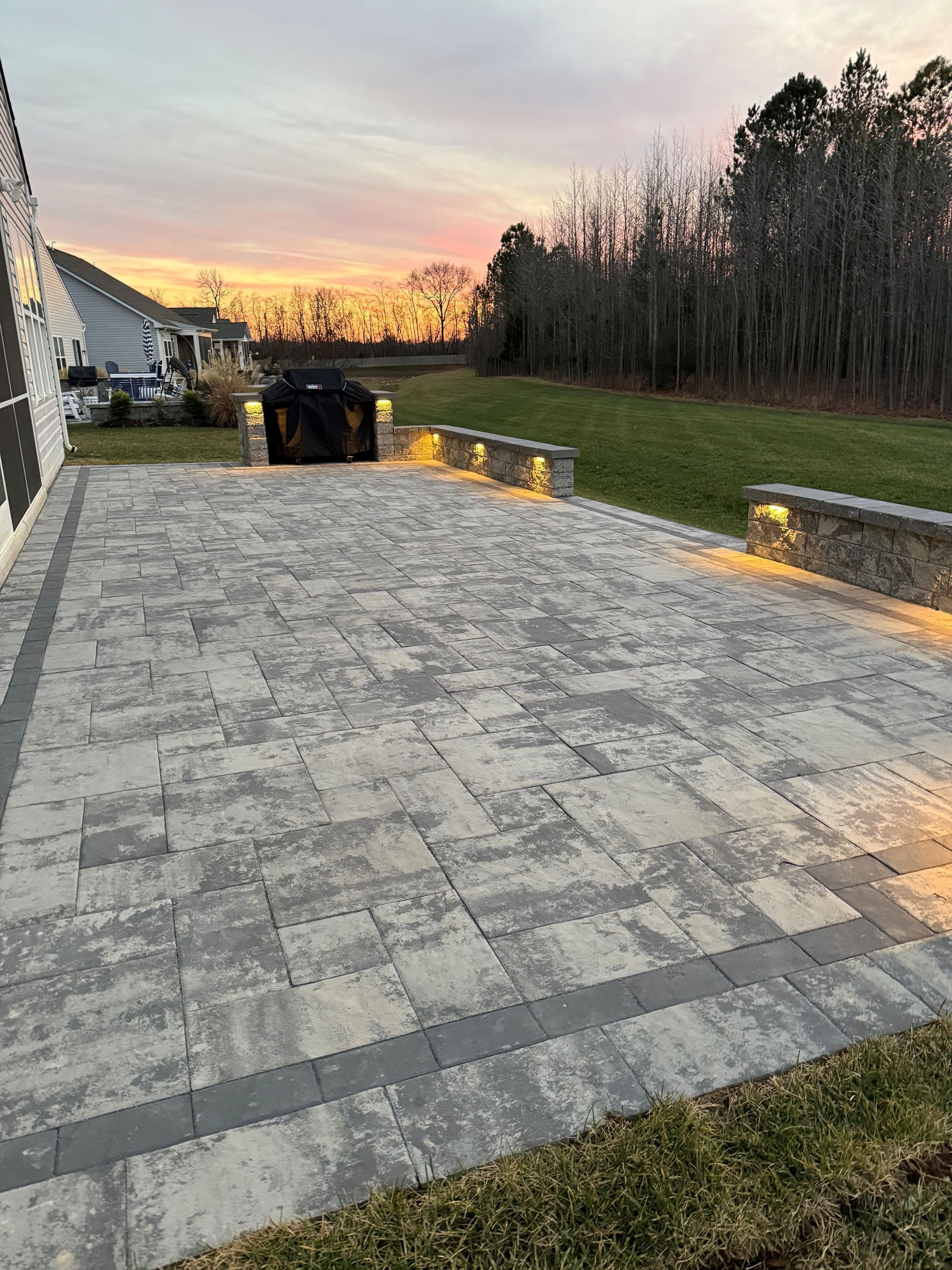A brick driveway leading to a house with a sunset in the background.