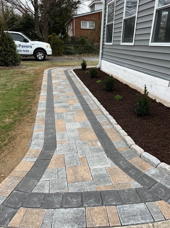 A brick walkway leading to a house with a truck parked in the background.
