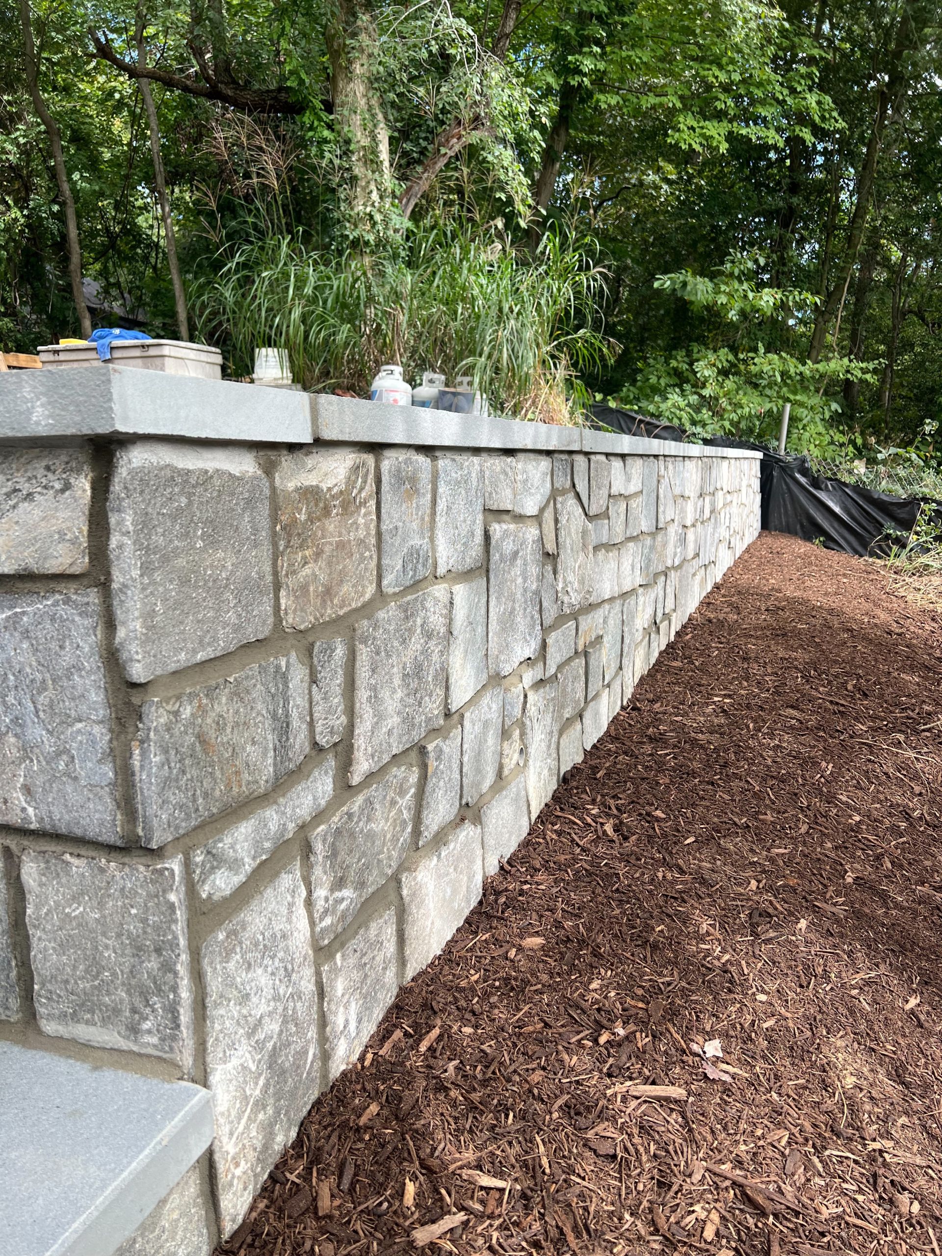 A stone wall is being built next to a pile of mulch.