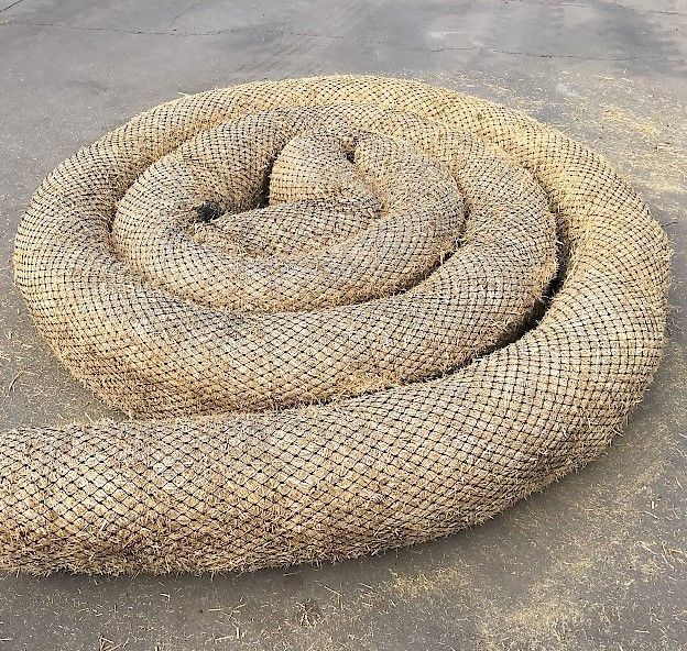 Coiled, cylindrical coir fiber erosion control log on a concrete surface. 