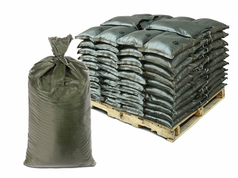 A single, tied-up green sandbag stands next to a pallet stacked high with dozens of similar sandbags.