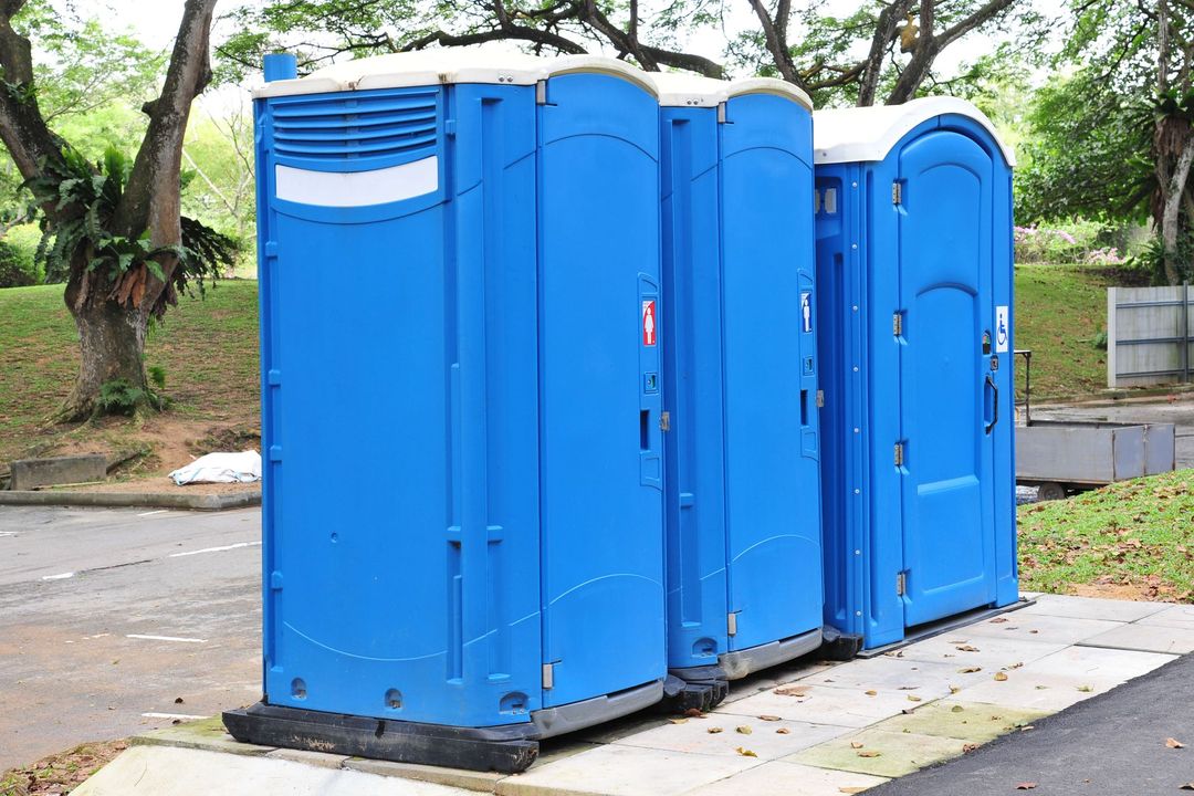 Three blue portable toilets lined up outdoors