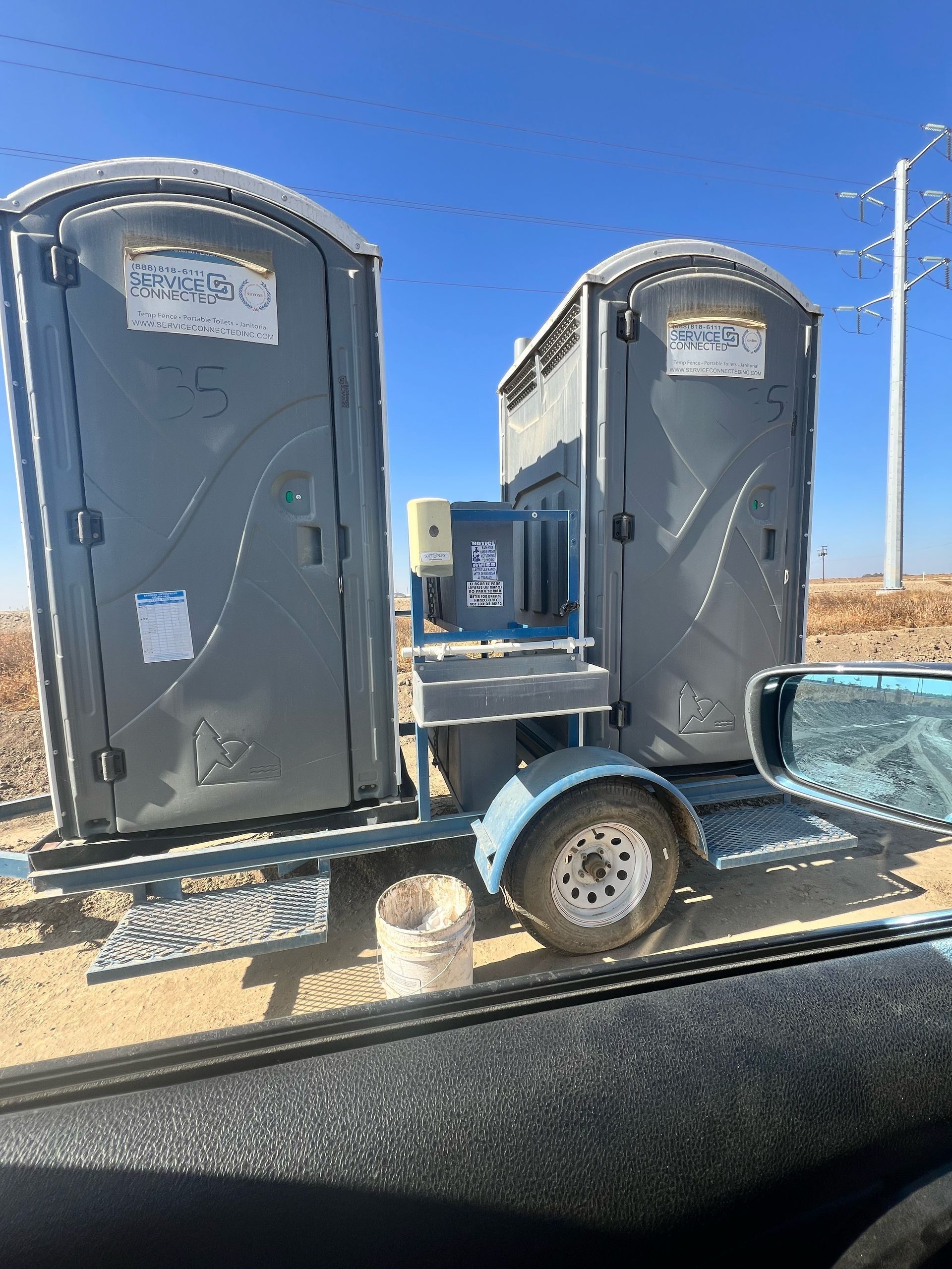 Two portable toilets on a trailer, with a handwashing station in between.