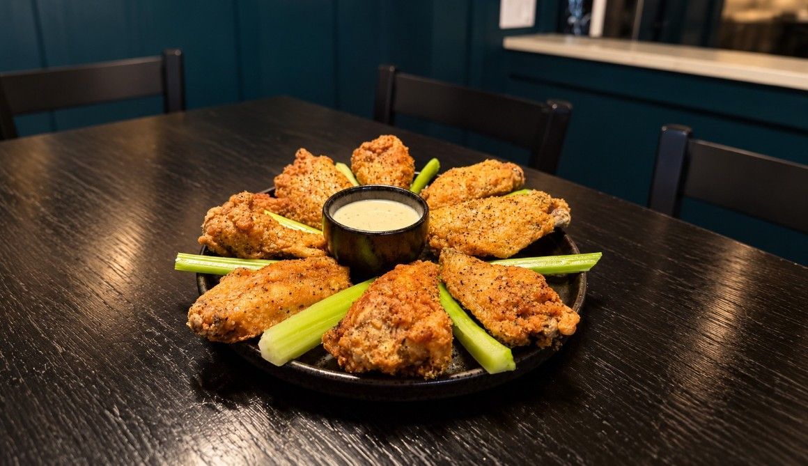Plate of fried chicken wings with celery sticks and dipping sauce on a dark table