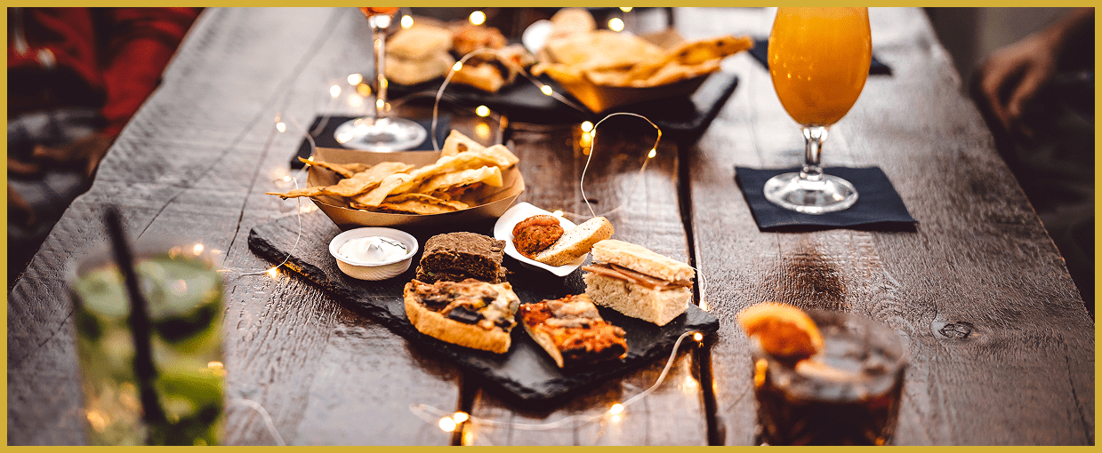 Appetizers and drinks on a rustic wooden table, including crostini, dips, and orange cocktails