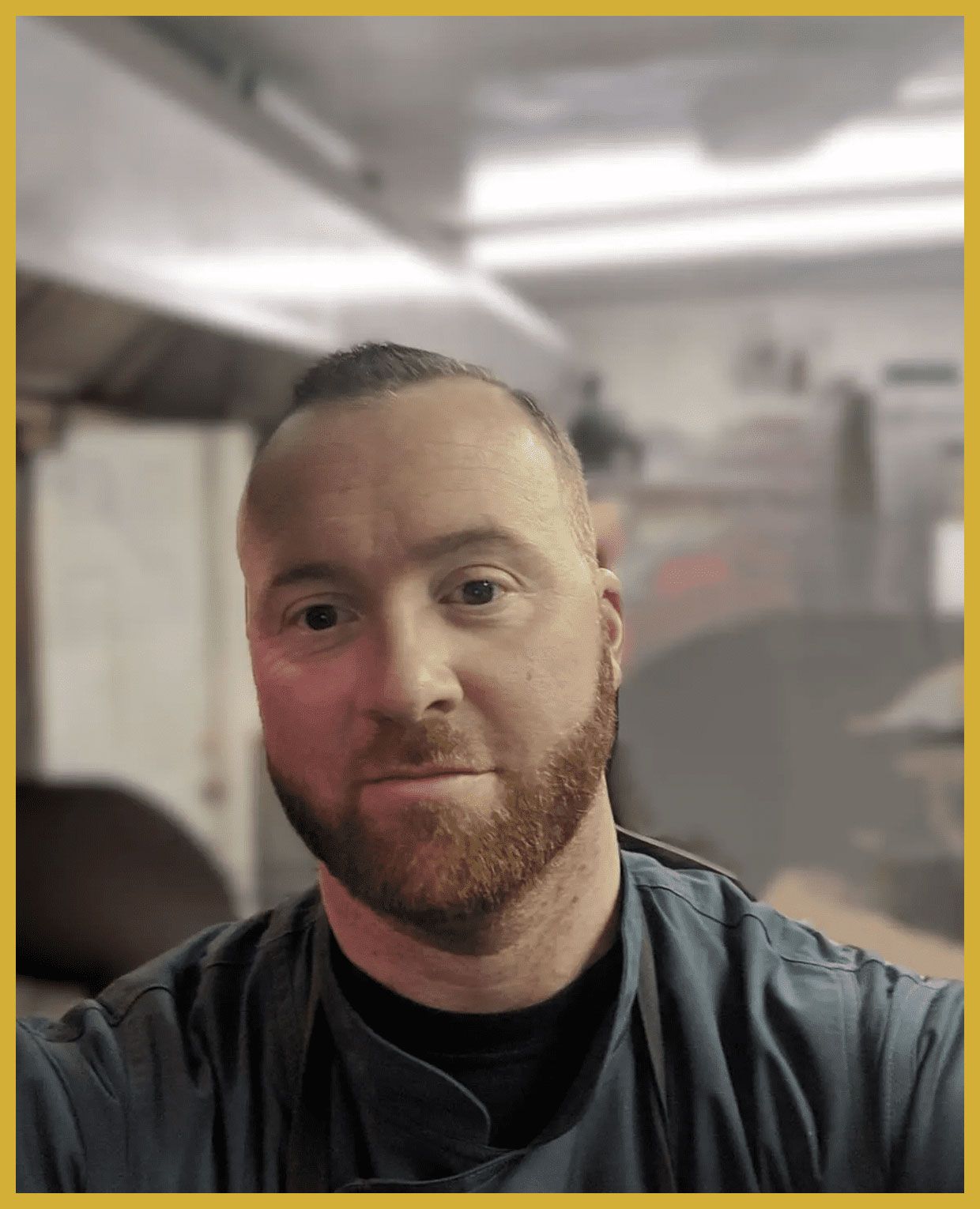 Man indoors taking a selfie, wearing a dark shirt with a blurred room in the background.