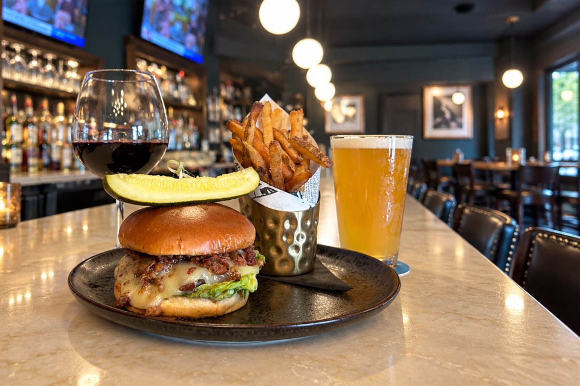 Burger and fries on a bar table with a pint of beer in a cozy restaurant.
