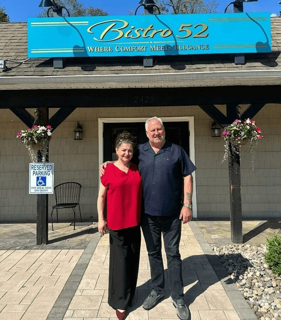 Two people standing outside Bistro 52 under a blue sign, smiling in front of the entrance