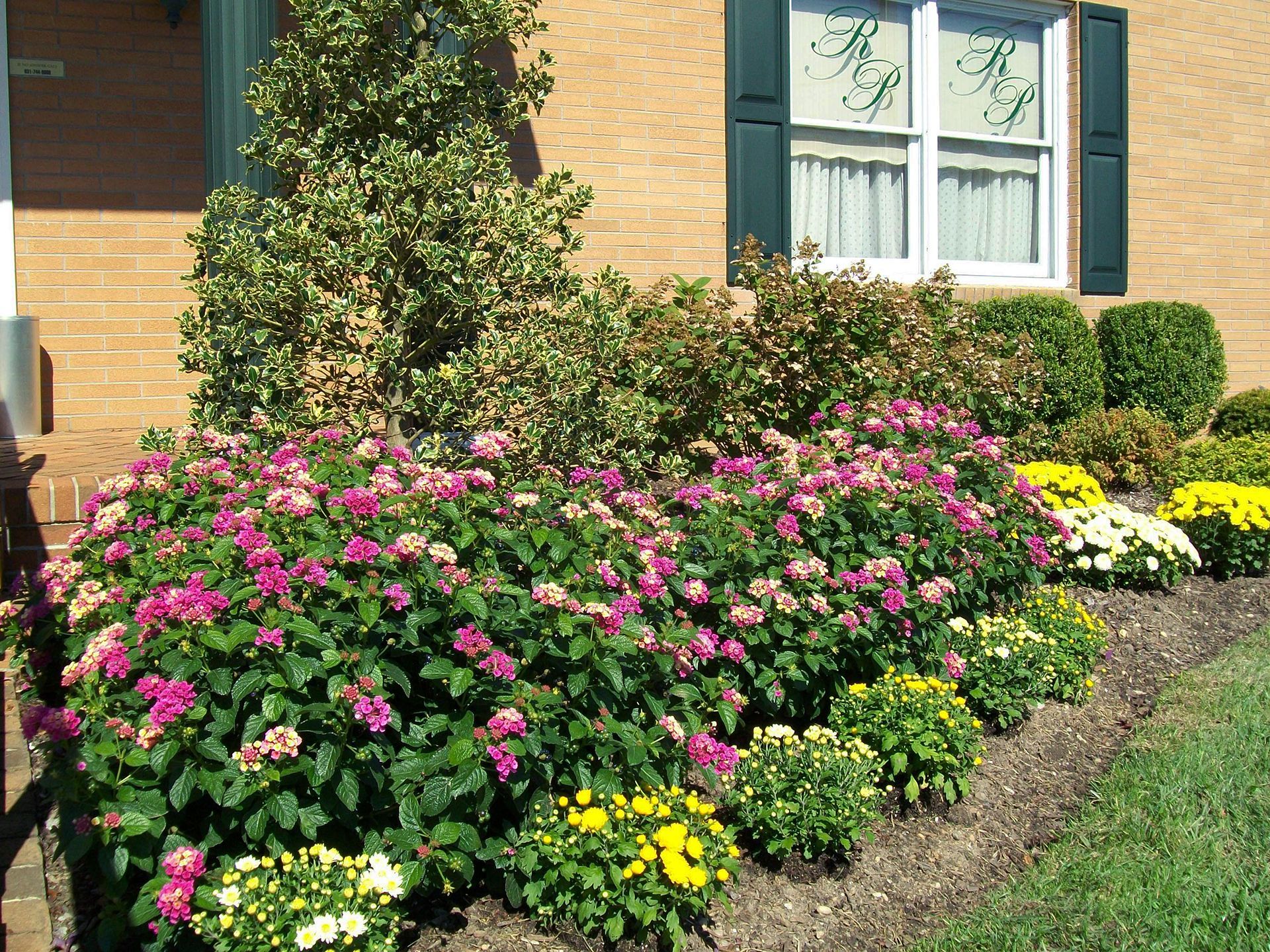 A brick house with pink and yellow flowers in front of it
