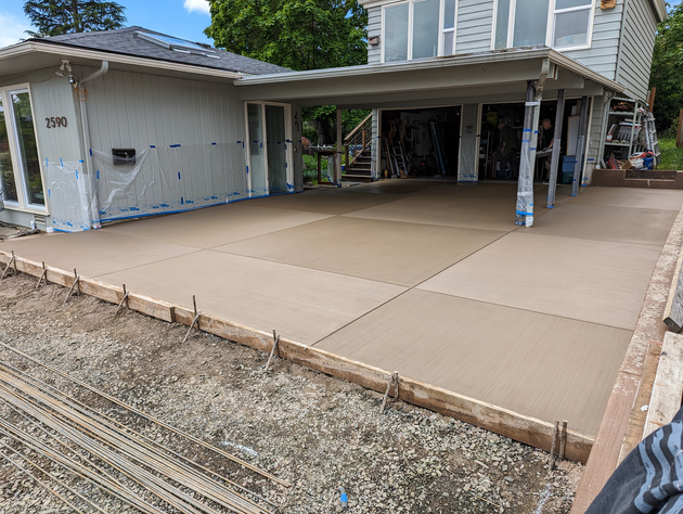 Concrete driveway and carport beside a house, with gravel in the foreground.