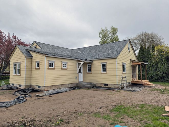Yellow house with a dark roof and unfinished landscaping on a cloudy day