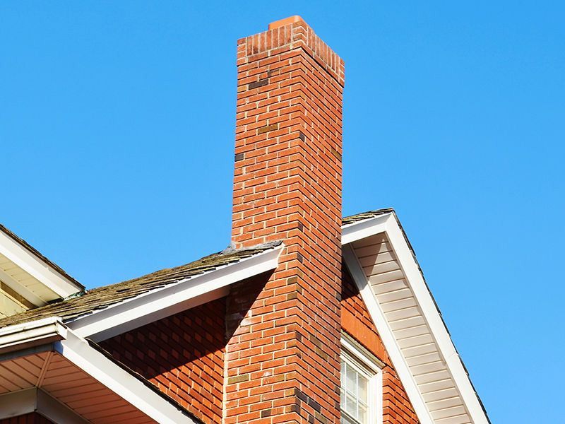 A brick chimney on top of a house with a blue sky in the background