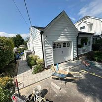 A white house with a garage and a wheelbarrow in front of it.