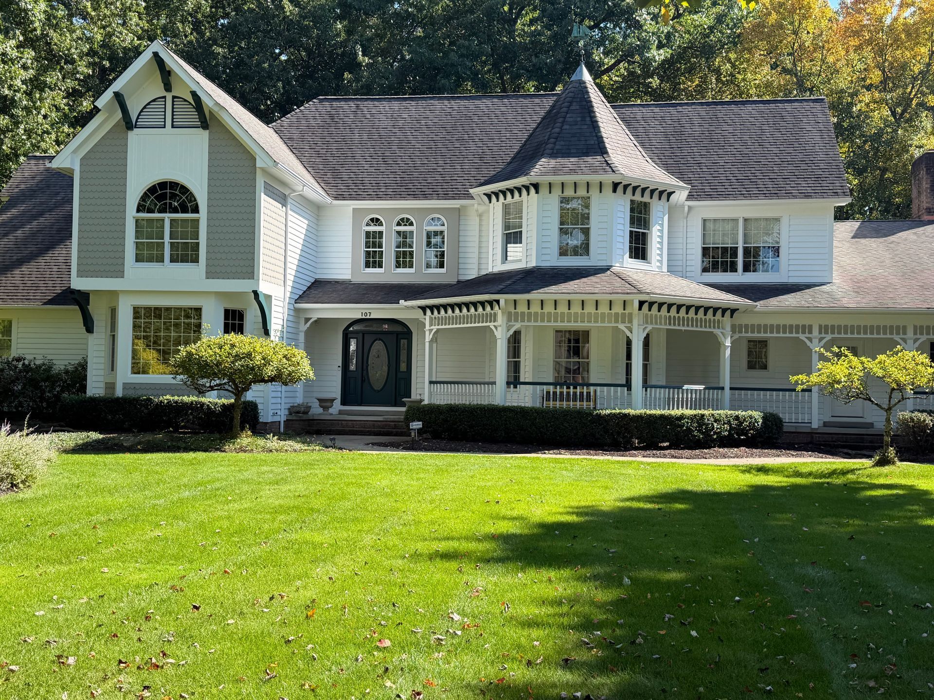Large white suburban house with a front porch, gabled roof, and a green lawn in front