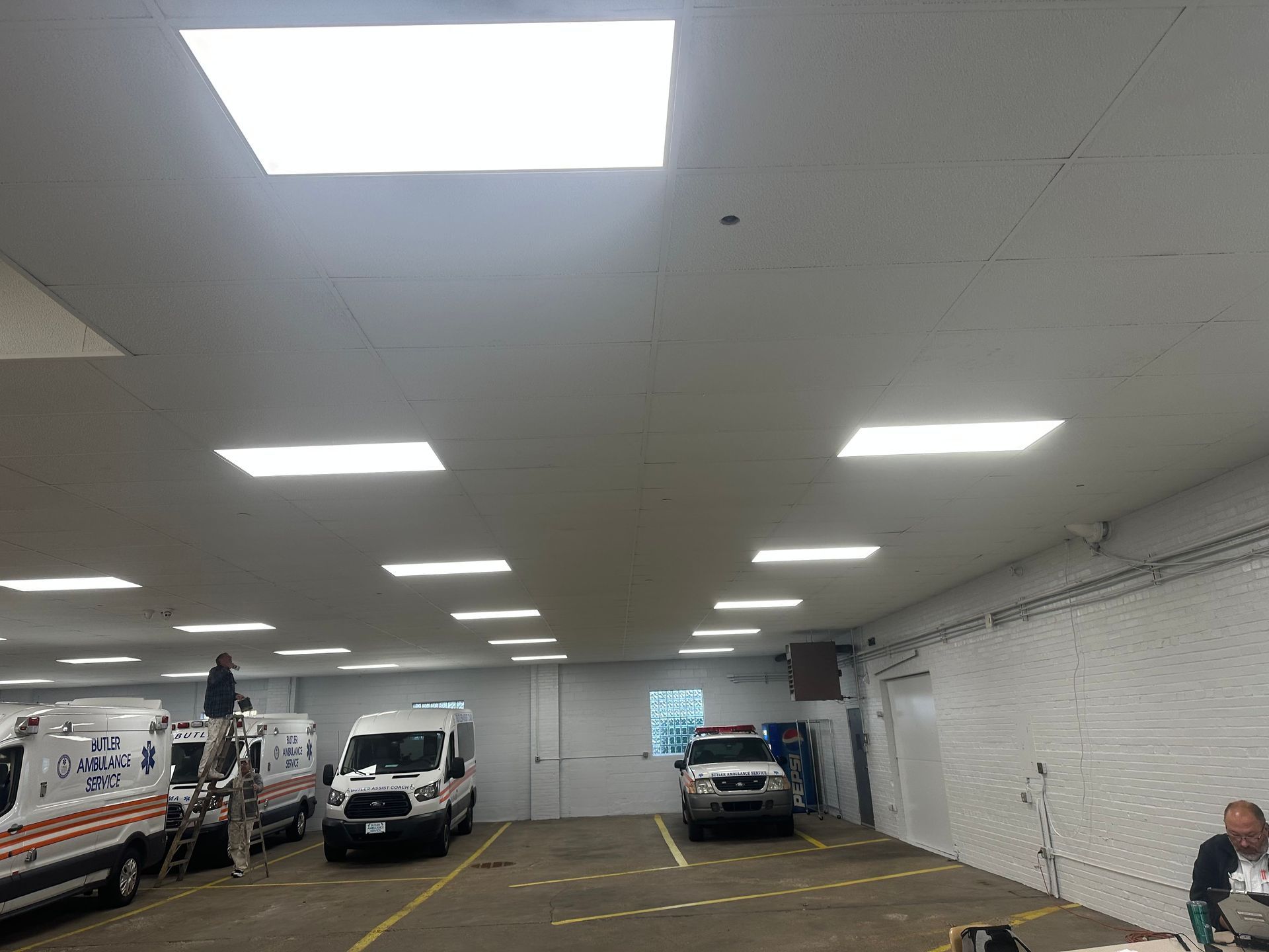 Inside a warehouse with several service vans parked, bright ceiling lights.