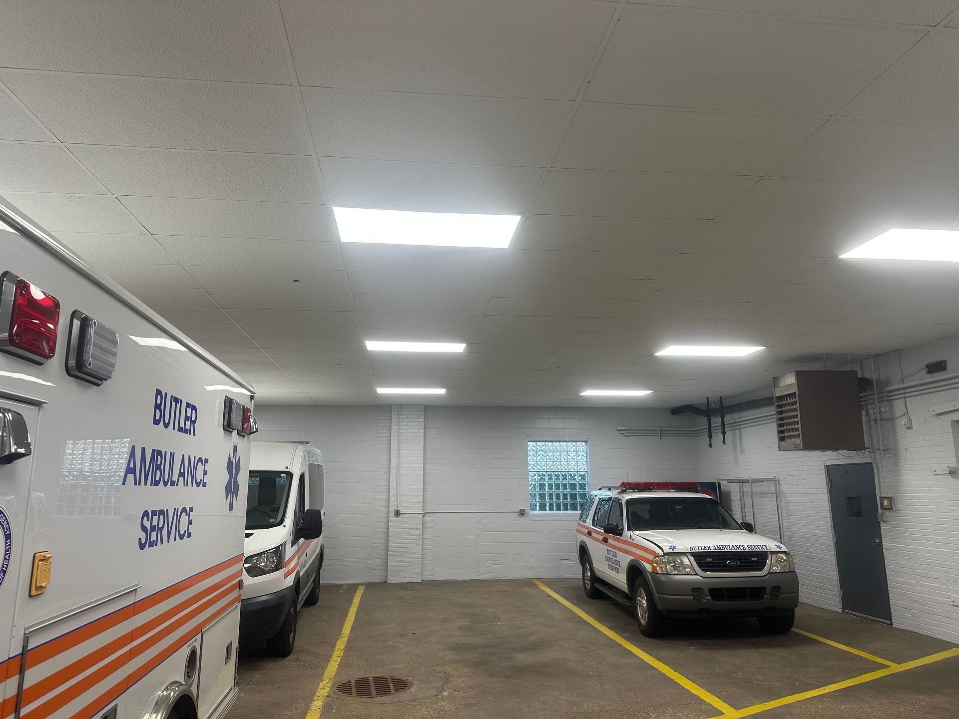 Inside a garage, two ambulances and an emergency vehicle are parked, with overhead lighting.