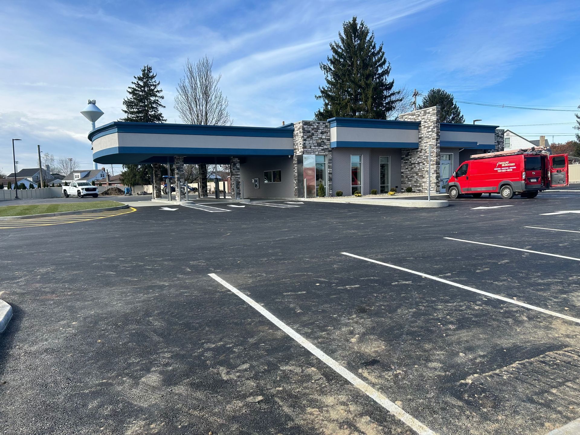 Exterior view of a newly constructed bank with a dark asphalt parking lot and red service vehicle.