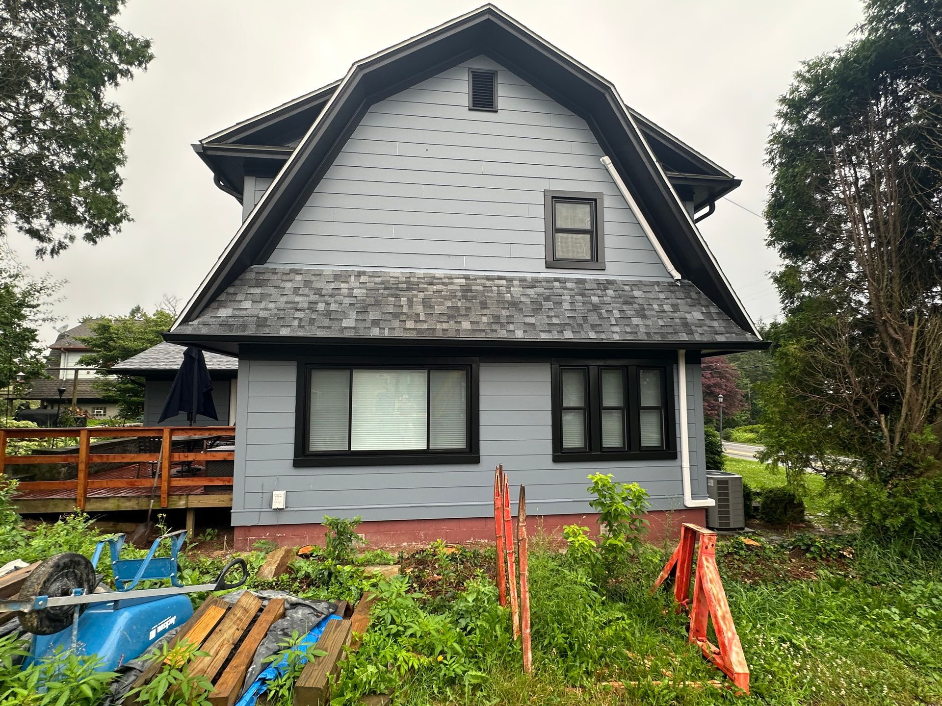 A gray house with a black roof and a wooden deck