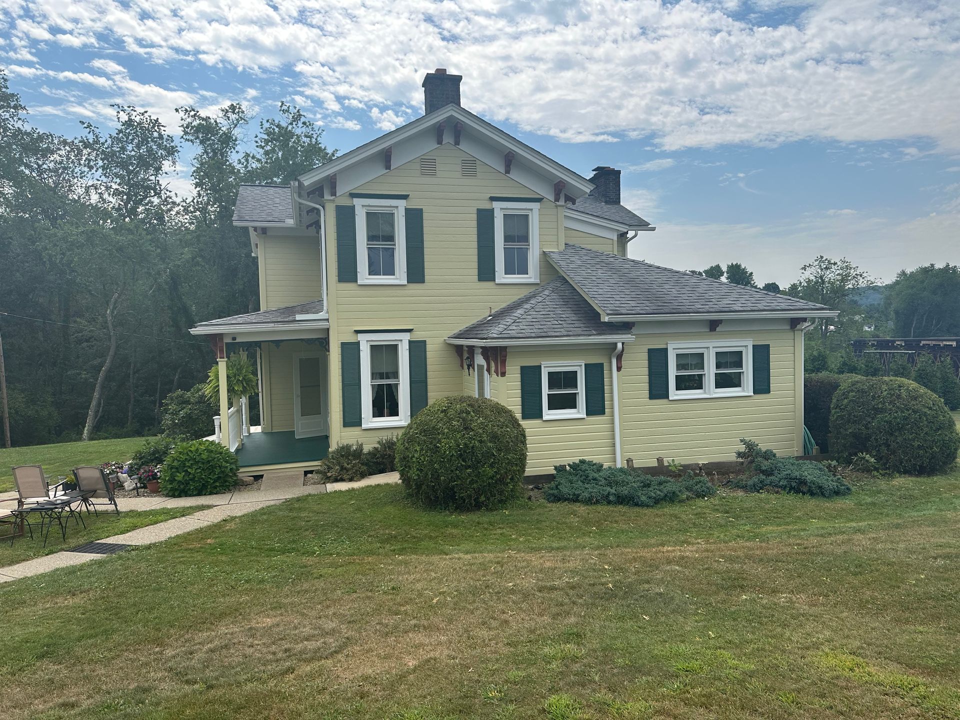 Yellow two-story house with green shutters and gray roof on a grassy lawn.