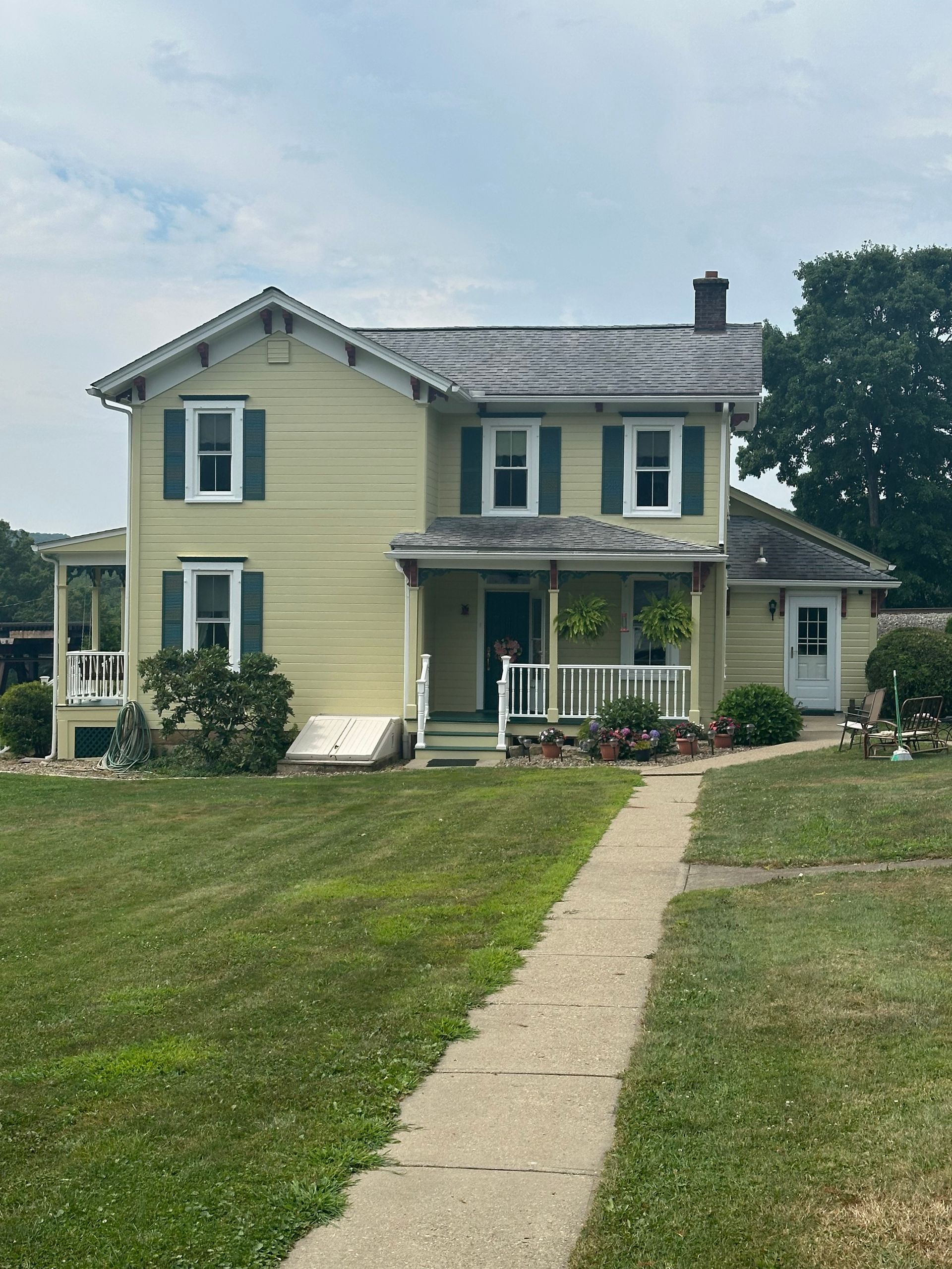 Two-story yellow house with green shutters and a concrete path leading to the front porch.