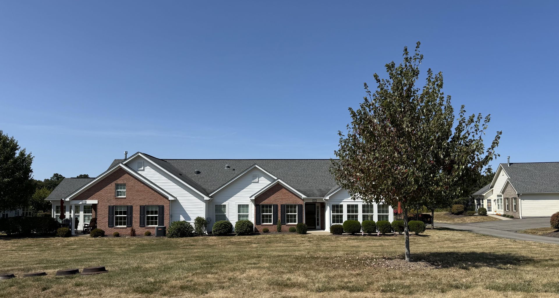 A one-story brick and white house under a blue sky; a tree is in the foreground.