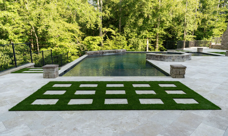 Backyard pool with stone patio, turf, and surrounding trees.