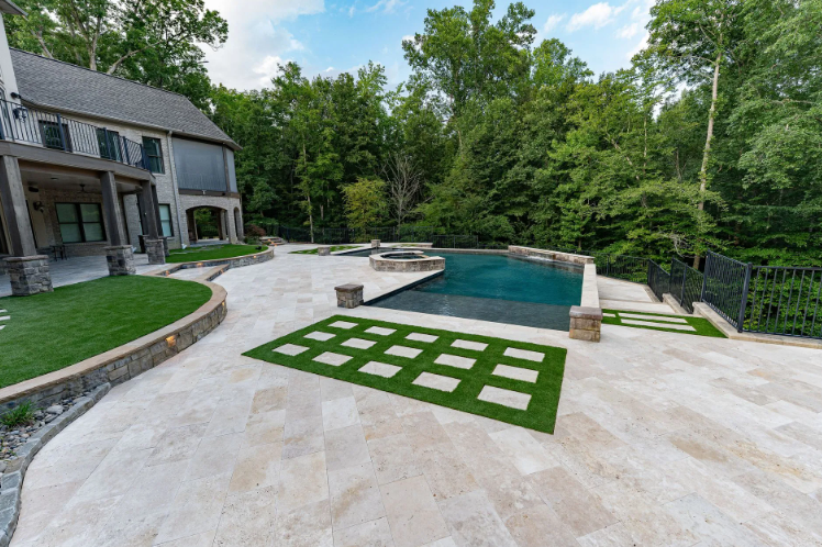 Luxury backyard with pool, patio, and house. Green lawn, stone pavers, and lush trees.