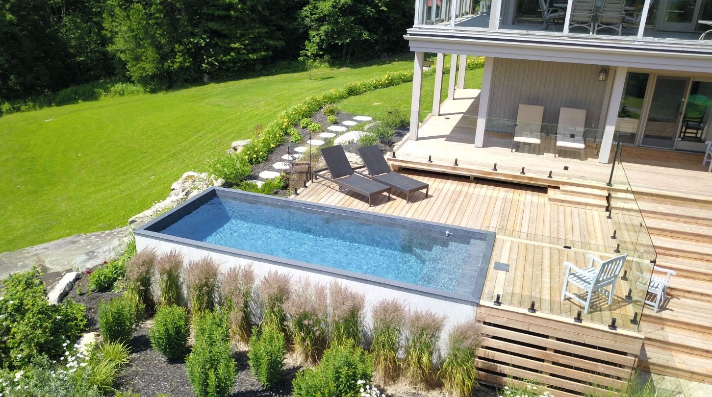 Backyard pool deck with lounge chairs beside a modern house and green lawn