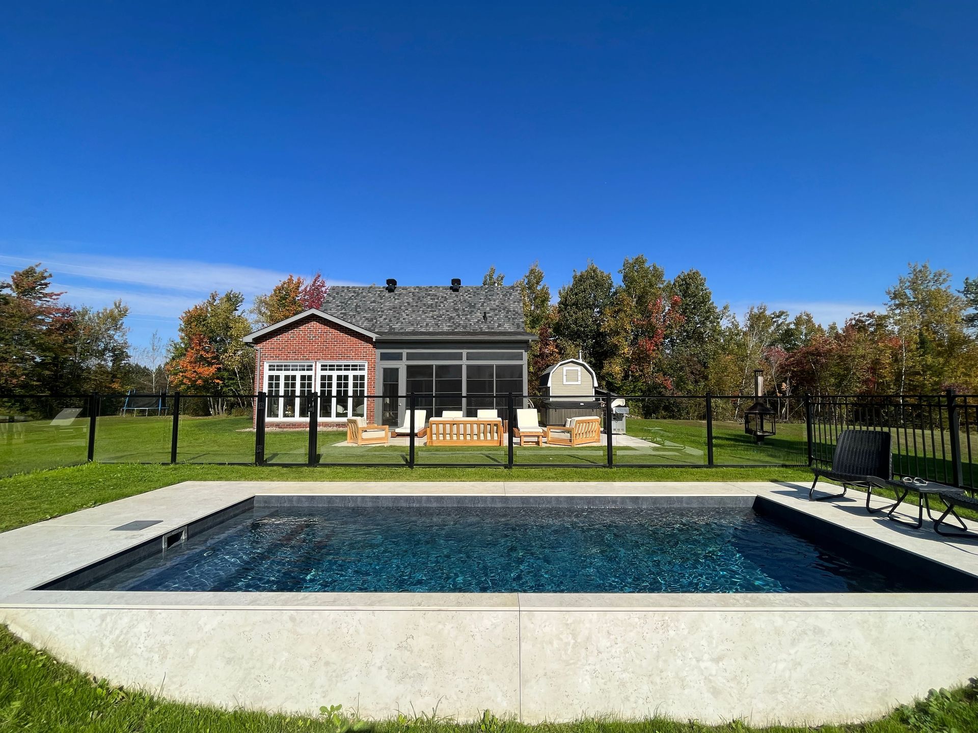 Modern house with a backyard pool, patio chairs, and autumn trees under a clear blue sky