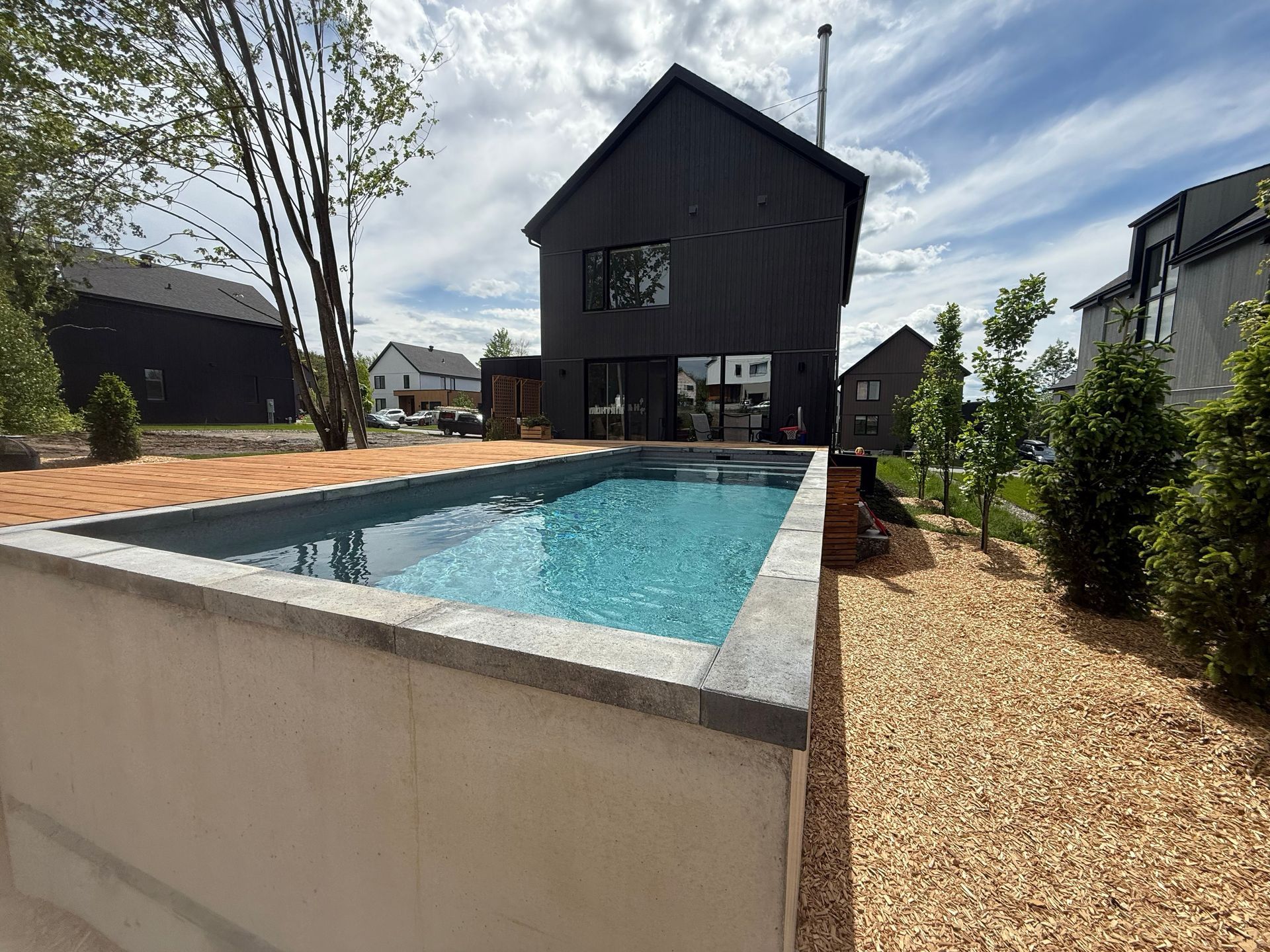Modern house with a long rectangular pool and gravel landscaping under a partly cloudy sky