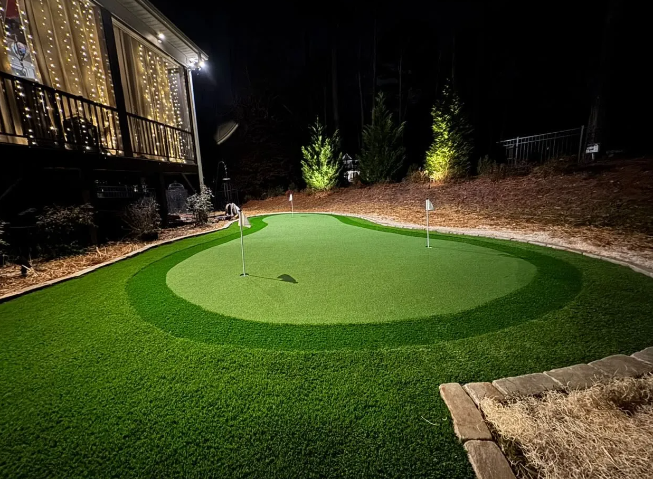 A backyard putting green at night, lit up with spotlights.