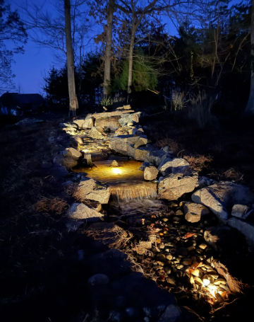 Lit stone waterfall in a dark outdoor setting, water flowing over rocks.