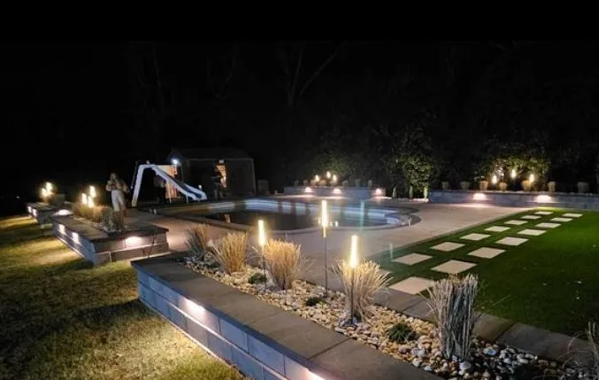 Nighttime illuminated backyard with pool, landscaping, and decorative lighting.