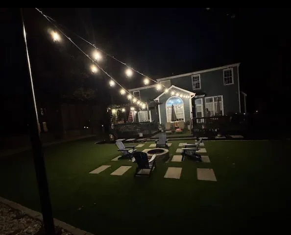 Backyard at night with string lights, fire pit, seating, and a house.
