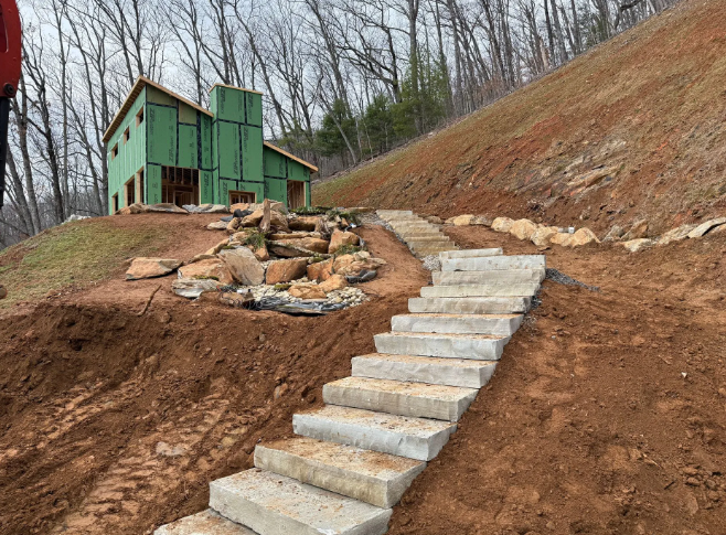 Concrete steps on a steep hillside lead to a building under construction. Red-brown earth surrounds.