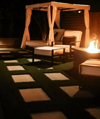 Outdoor lounge area at night with a fire pit, gazebo, and stepping stones.