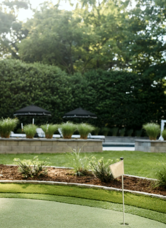 A backyard with a putting green, hedges, umbrellas, and a pool. Green and neutral tones.