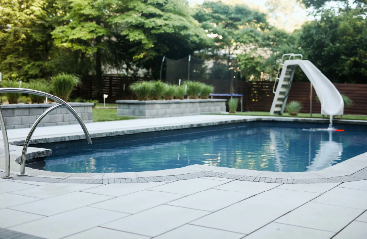 Swimming pool with slide, stone patio, and raised garden beds in a backyard.