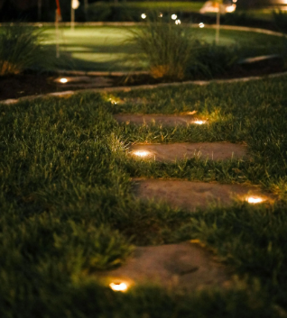 Stepping stones illuminated by ground lights lead to a putting green at night.