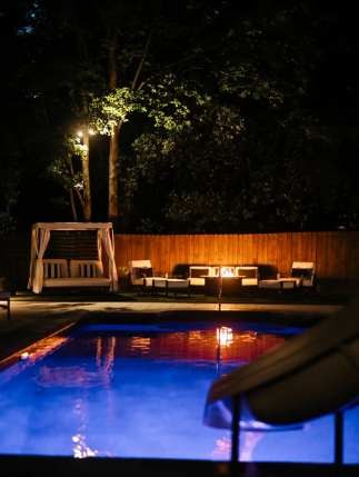 Nighttime pool scene with a slide, seating area, and string lights.