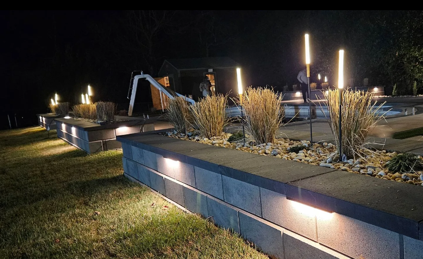 Nighttime landscape with illuminated retaining walls, tall lights, and people in the distance.