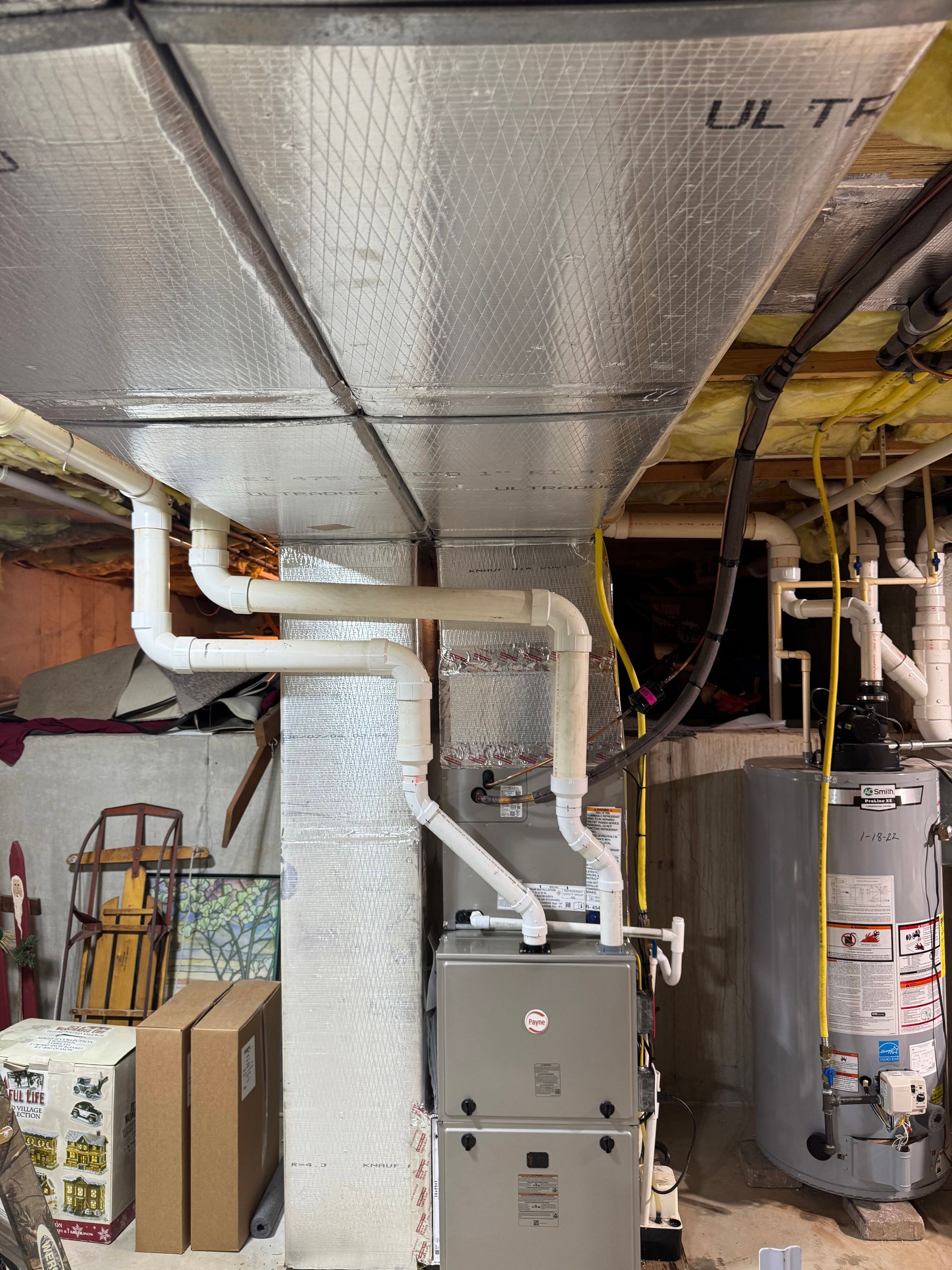 Basement utility room with insulated ducts, white PVC pipes, and a furnace beside a water heater.