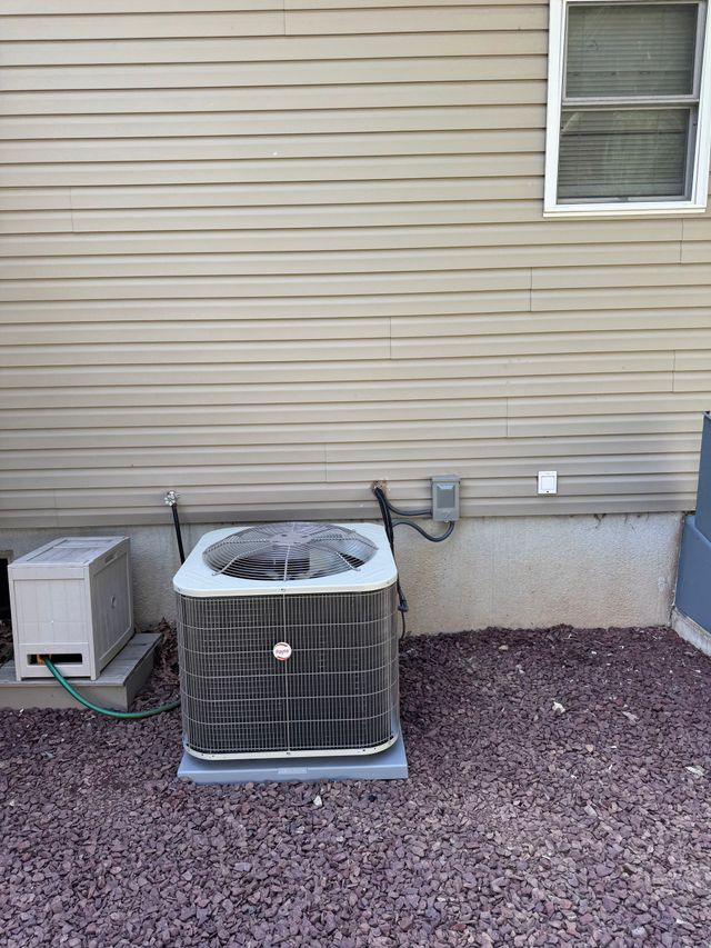 Outdoor HVAC unit beside a beige house wall with a window and utility box on gravel.
