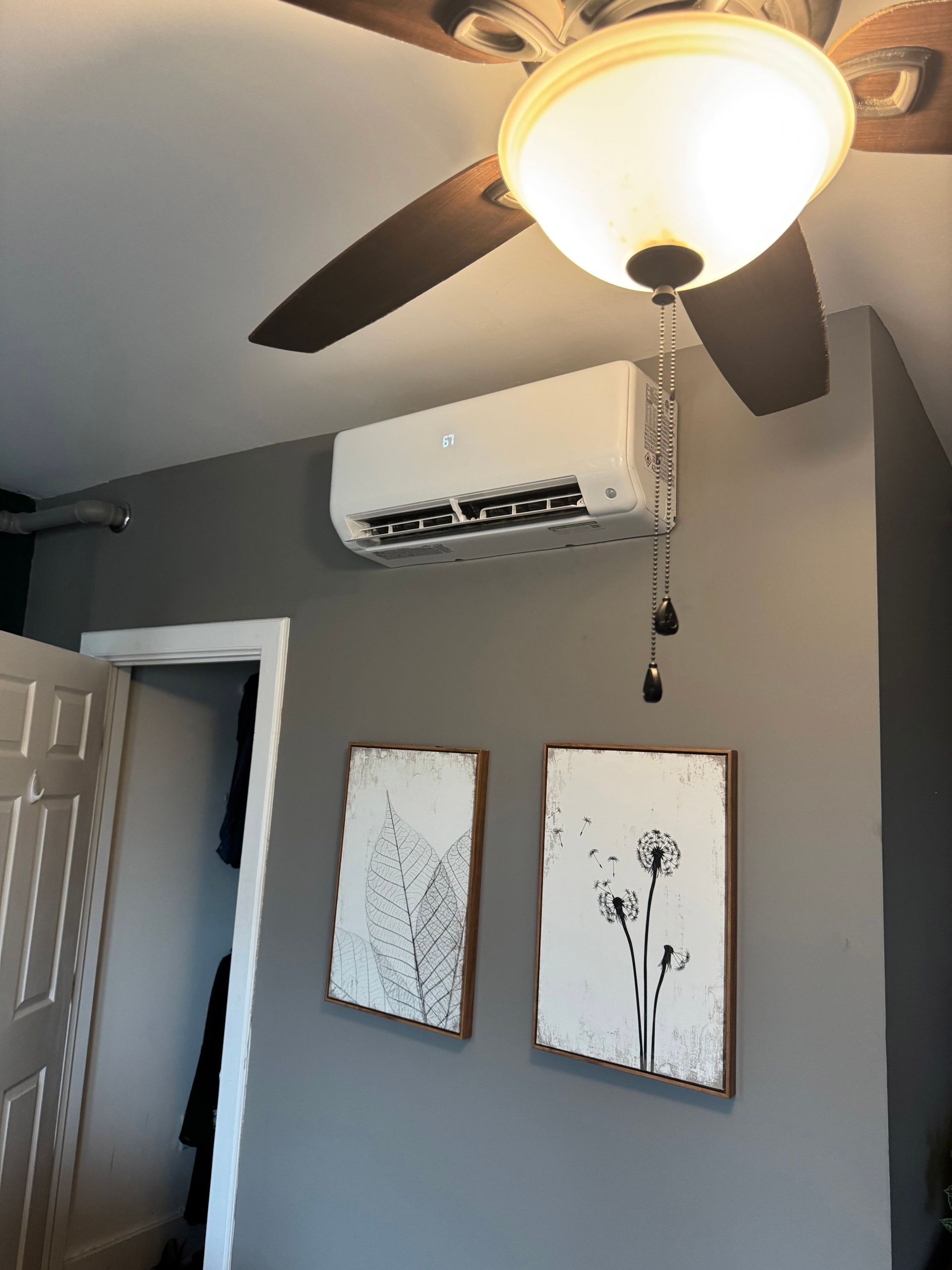 Gray bedroom wall with air conditioner, ceiling fan, and two framed floral prints above an open doorway