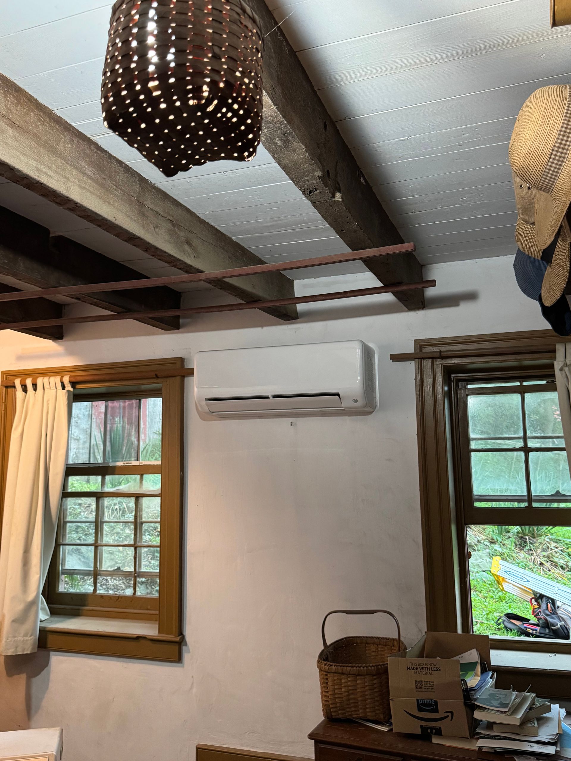 Cozy room with white walls, wooden windows, ceiling lights, and an air conditioner above stacked boxes.