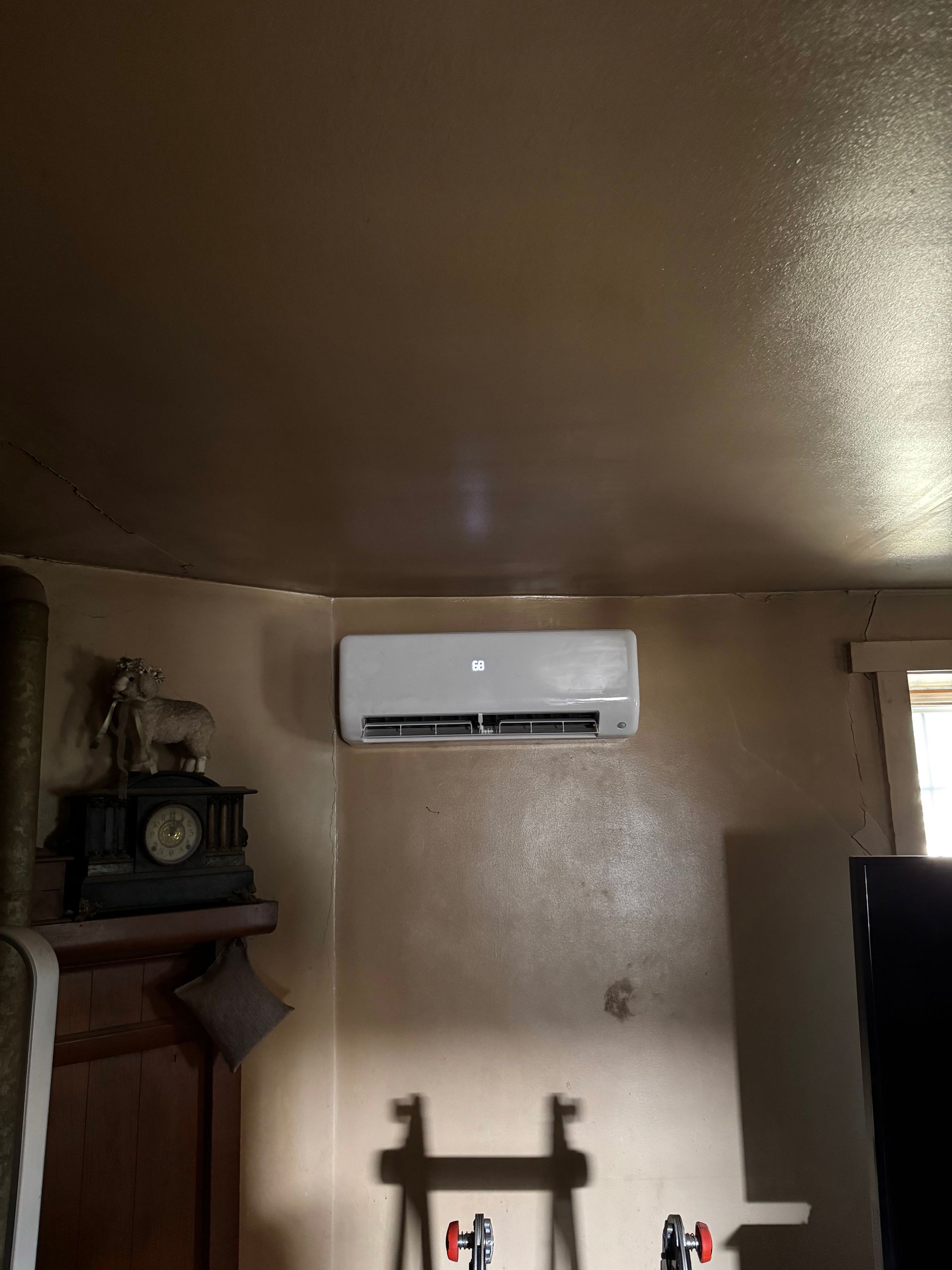 Dim room interior with a wall-mounted white air conditioner above a wooden cabinet and shelf.